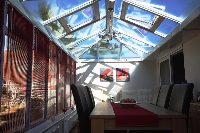 Bright conservatory with a glass roof, dining table, and red blinds