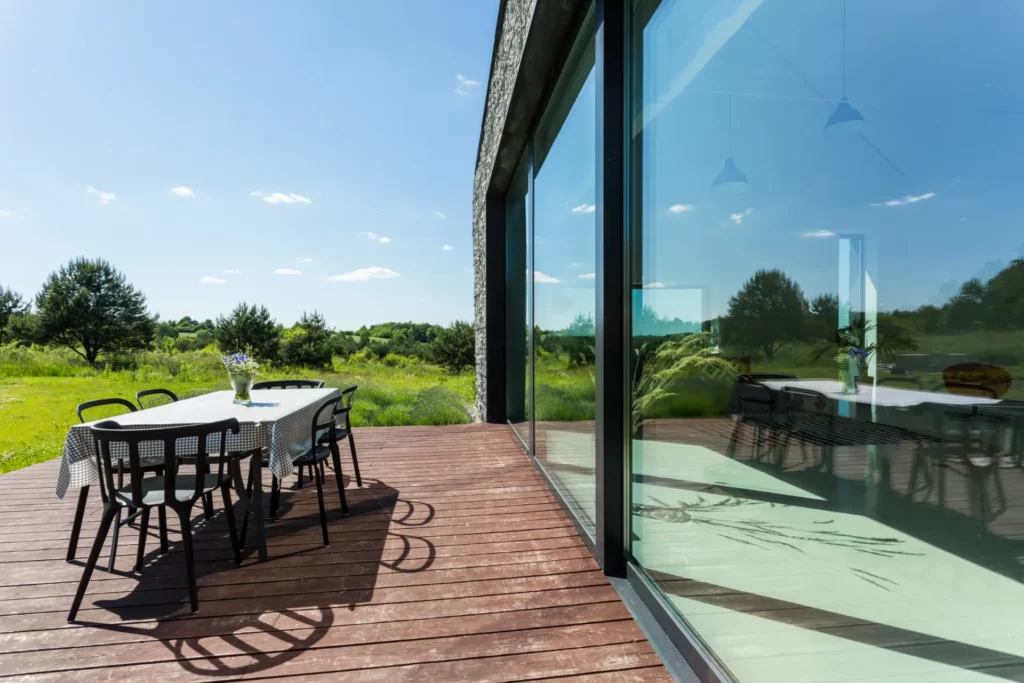 Modern glass sliding doors opening to a wooden deck with outdoor dining and scenic view