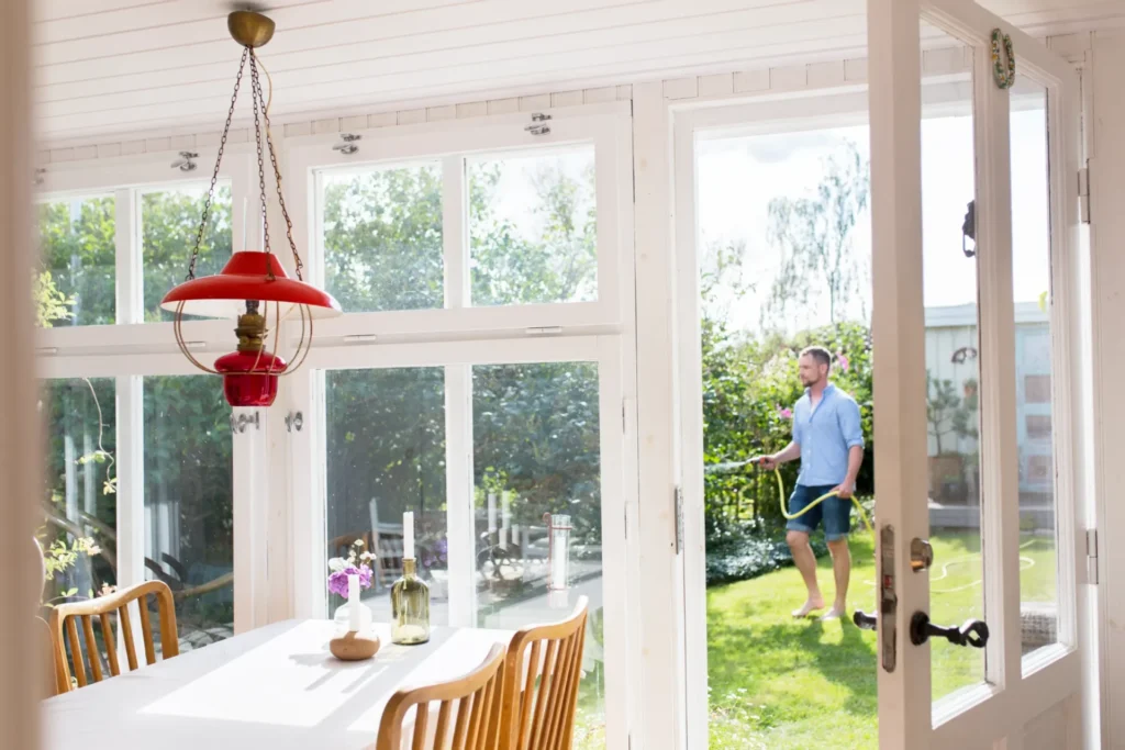 Bright dining room with white windows and a man watering the garden outside