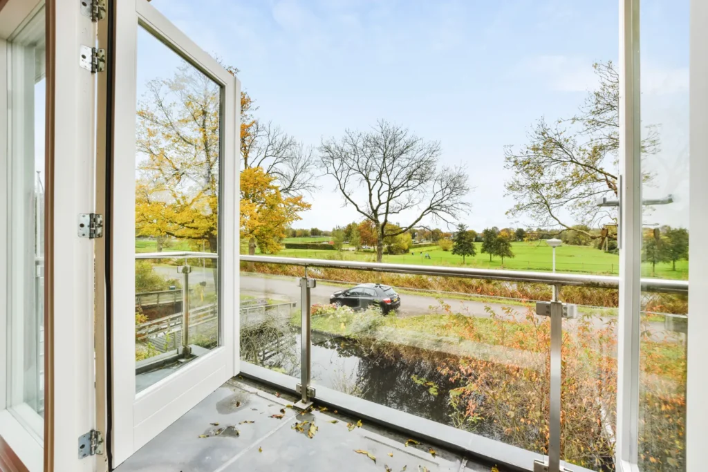 Open white sliding door with glass balcony and scenic view of trees and park